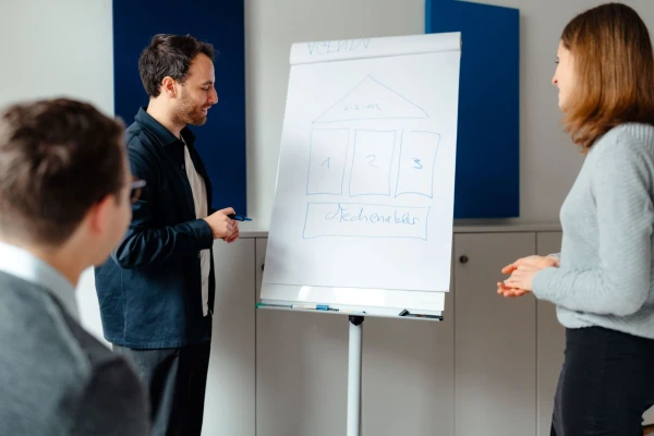 A man and woman stand together in front of a whiteboard, engaged in discussion or presentation.